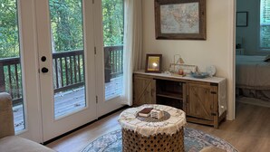 Habitación con un amplio ventanal corredero que da a una terraza, un taburete redondo de madera con cojín, una mesita con objetos decorativos y un mapa en la pared.