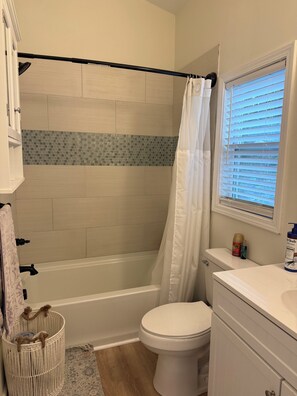 Ein Badezimmer mit Badewanne, Toilette und einem Fenster mit Jalousien.