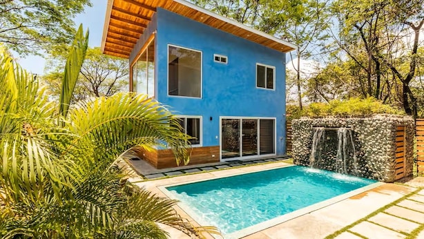 Uma casa moderna de dois andares com piscina, rodeada por vegetação exuberante e uma cascata.