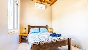 Quarto com cama de madeira, janela e mesa de cabeceira com abajur.