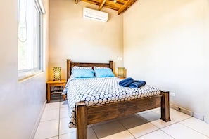 A bedroom with a wooden bed, a window, and a nightstand with a lamp. - Fully equipped house 5 minutes from the beach. Perfect for families or groups of friends. (Nosara)