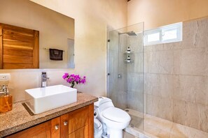 A bathroom with a white sink, wooden vanity, a toilet, and a glass-enclosed shower. - Fully equipped house 5 minutes from the beach. Perfect for families or groups of friends. (Nosara)