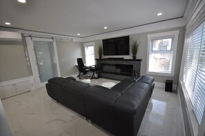 Een moderne woonkamer met een zwarte leren bank, een flatscreen televisie, een open haard en een schuifpui naar een balkon.