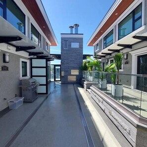 A modern building with a central tower, a covered outdoor area with potted plants, and a grill. - Beautiful Bright 3 Bed Townhouse (Vancouver)
