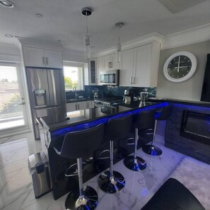 A modern kitchen with a central island, bar stools, a microwave, and a clock on the wall. - Beautiful Bright 3 Bed Townhouse (Vancouver)