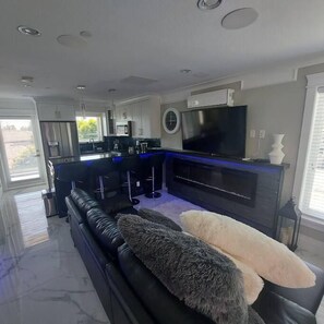 Eine moderne Küche mit Flachbildfernseher, Einbauofen und Essbereich mit schwarzem Sofa und weichen Kissen.