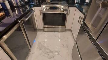 A modern kitchen with stainless steel appliances, a marble floor, and a black backsplash.