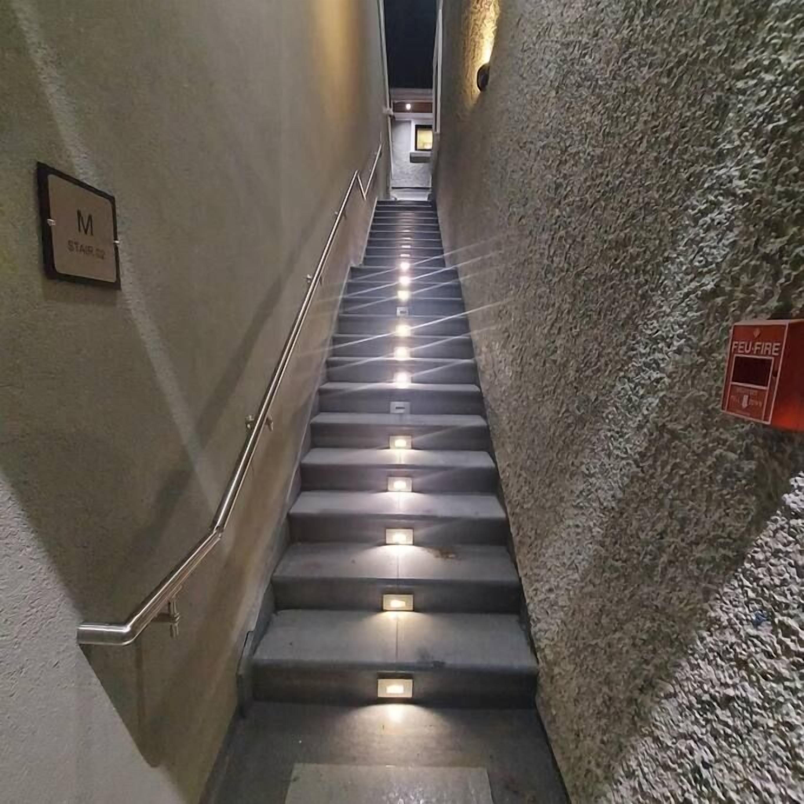 A stairwell with a handrail, a fire alarm, and a sign indicating the location.