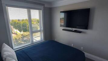 A bedroom with a bed, a window with blinds, a mounted TV, and a ceiling light.