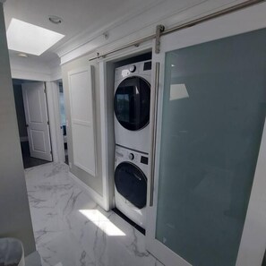 Una lavanderia con lavatrice e asciugatrice, una porta che dà su un'altra stanza e un pavimento in marmo.