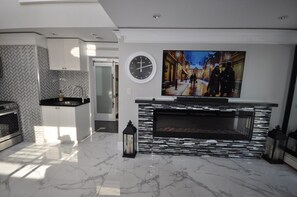 A modern kitchen with a fireplace, a clock, and a painting of a snowy street scene.