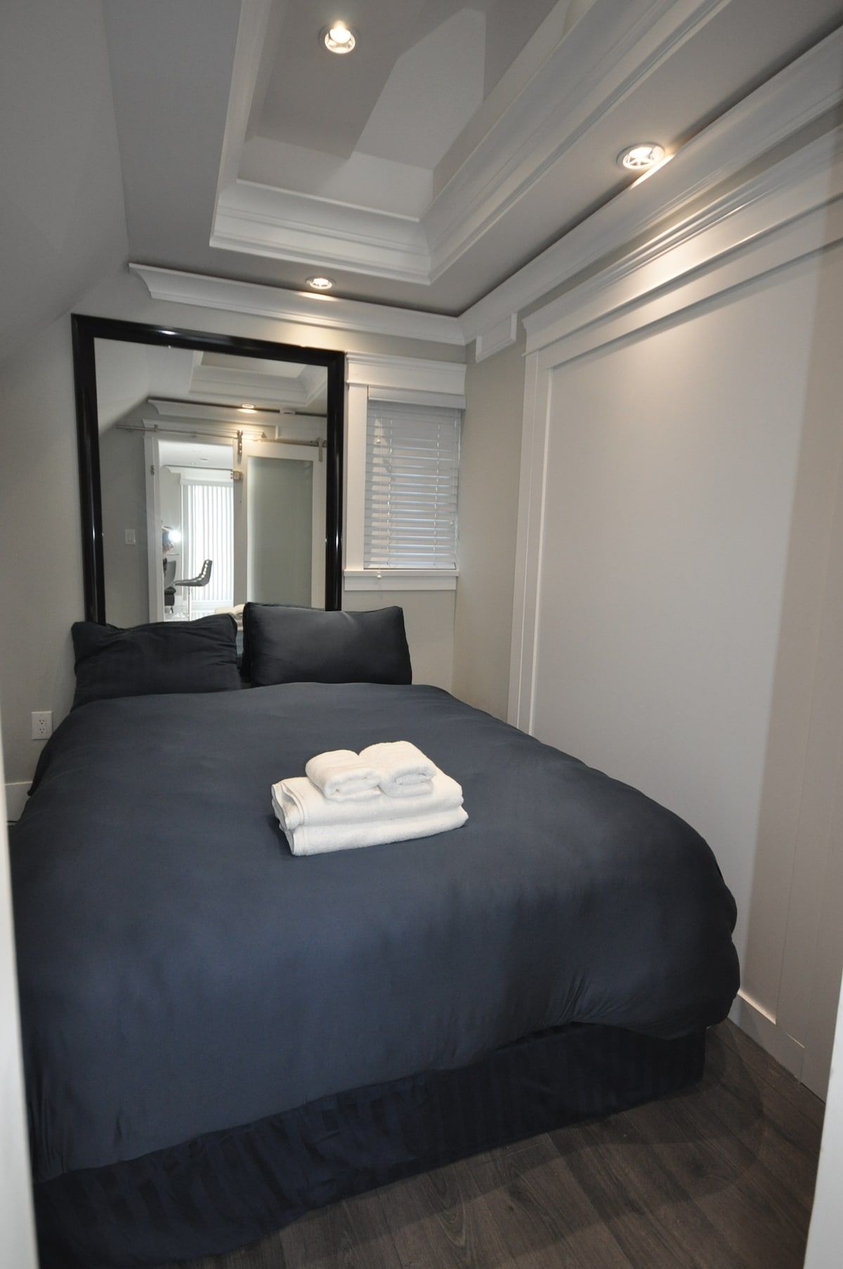 A hotel room with a large bed, a mirror, and a window with blinds.