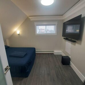 A small room with a bed, a television mounted on the wall, a window, and a heater.
