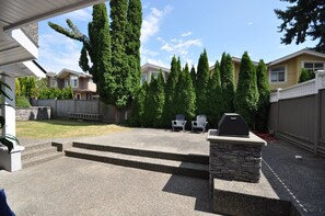 A backyard with a barbecue grill, outdoor seating, and a stone accent wall. - New Luxurious 3 Bedroom Kingsway Castle Suite (Burnaby)