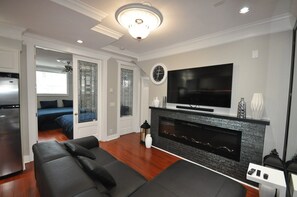 A modern living room with a fireplace, a flat-screen TV, and a sofa. - New Luxurious 3 Bedroom Kingsway Castle Suite (Burnaby)