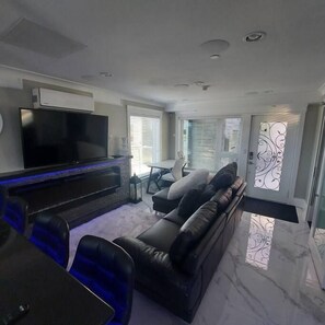 A modern living room with a flat-screen TV, a dark sofa, and a dining area with blue chairs. - Beautiful Luxurious 3 Bed Townhouse (Vancouver)