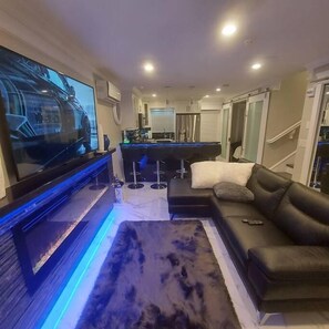 Una sala de estar moderna con un televisor de pantalla plana, una mesa de billar, un sofá y una zona de bar.