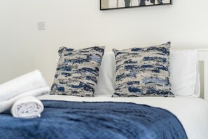 A bed with white bedding and two pillows with a blue and white pattern.
