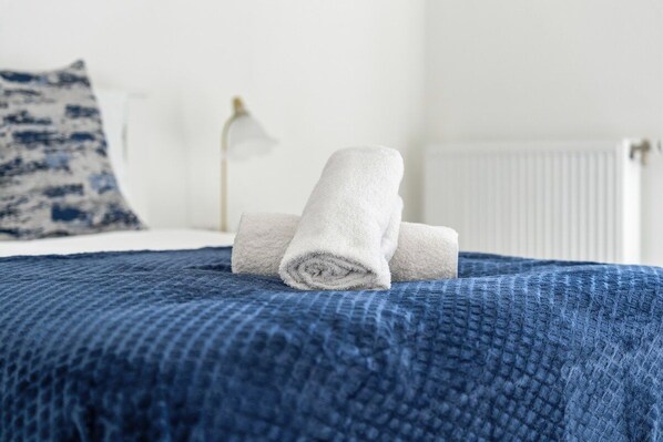 A neatly made bed with a blue blanket and rolled white towels.