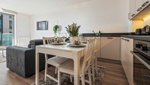 Et moderne køkken med hvide skabe, et spisebord dækket til fire personer, og et stort vindue der giver naturligt lys.