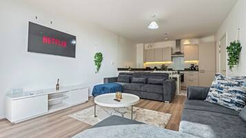 A modern living room with a grey sofa, a coffee table, and a flat-screen TV mounted on the wall.