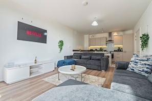 A modern living room with a grey sofa, a coffee table, and a flat-screen TV mounted on the wall.