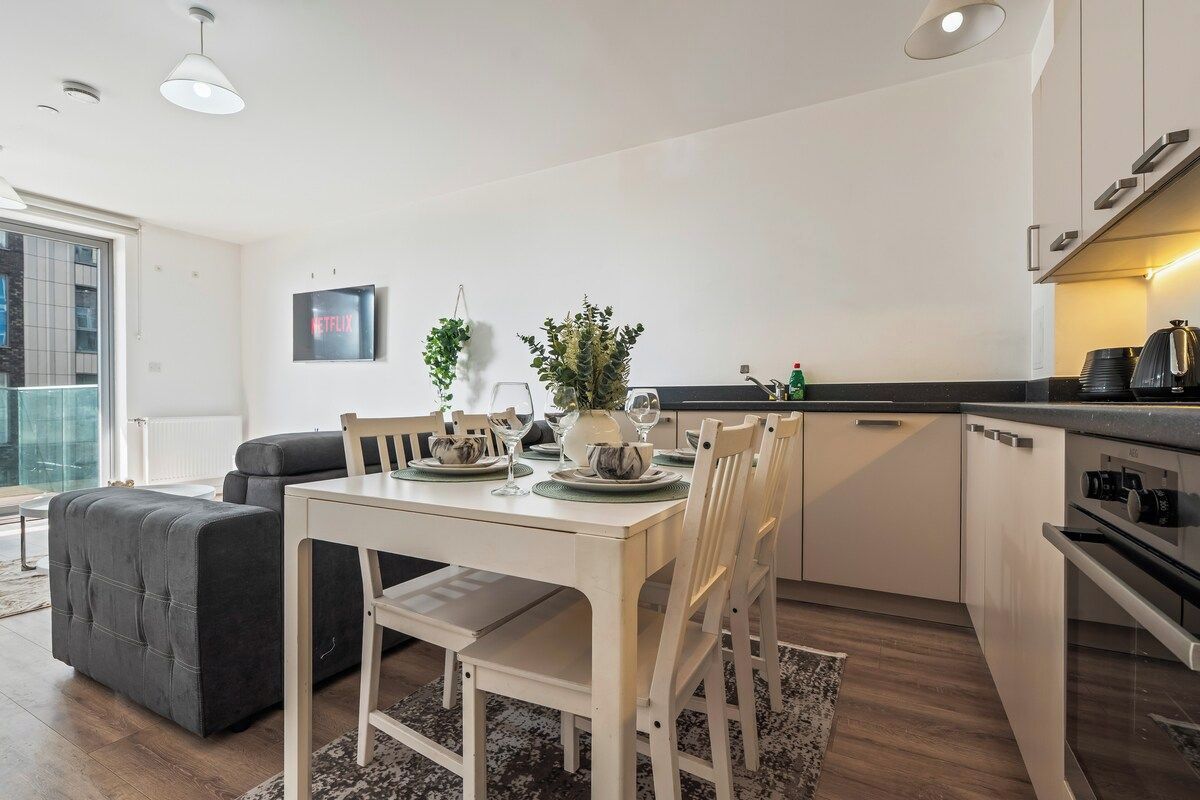 A modern kitchen with white cabinetry, a dining table set for four, and a grey sofa in the living area.