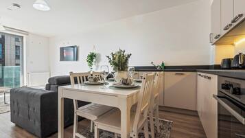 A modern kitchen with white cabinetry, a dining table set for four, and a grey sofa in the living area.
