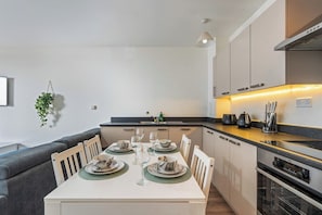 A modern kitchen with a dining area, featuring a built-in oven, a sink, and a countertop with kitchen appliances.