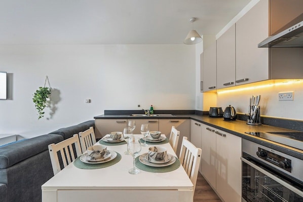A modern kitchen with a dining area, featuring a built-in oven, a sink, and a countertop with kitchen appliances.