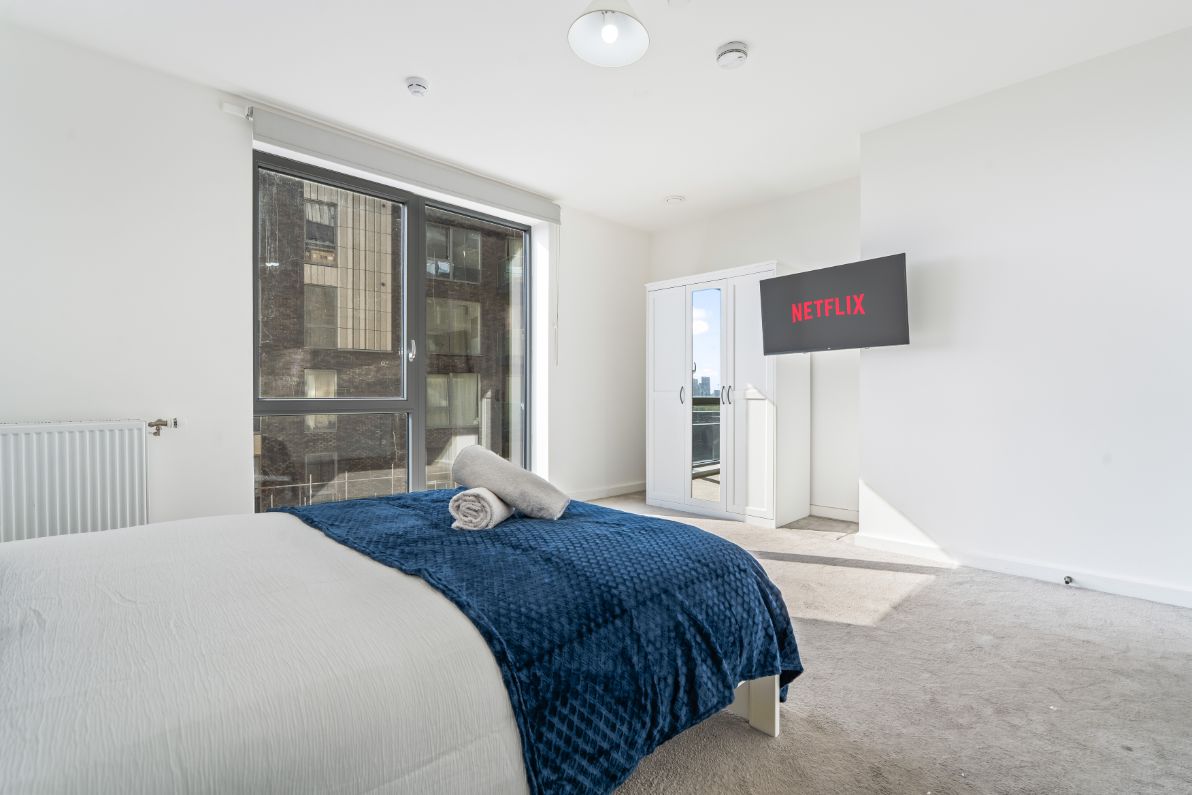 Quarto com cama, televisão fixada na parede e porta de vidro corria para uma varanda.