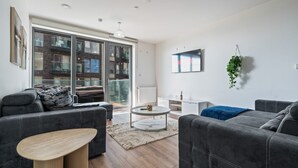 En moderne stue med grå sofaer, et sofabord og en stor skydedør, der fører ud til et udendørs område.