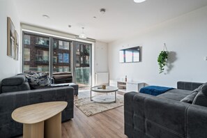 Sala de estar moderna com sofás cinzas, uma mesa de centro e uma grande porta de vidro deslizante que dá para uma área externa.