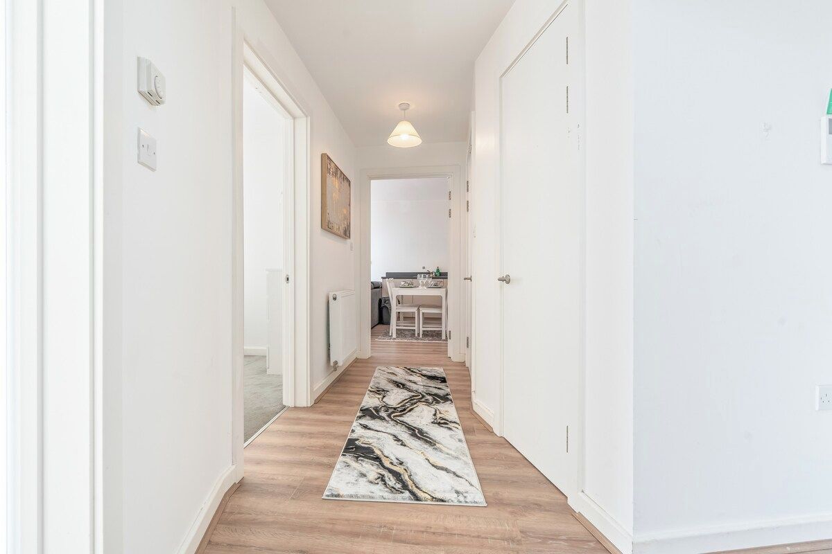 A hallway with a marble-patterned rug, white walls, and a ceiling light.