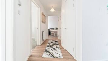 A hallway with a marble-patterned rug, white walls, and a ceiling light.