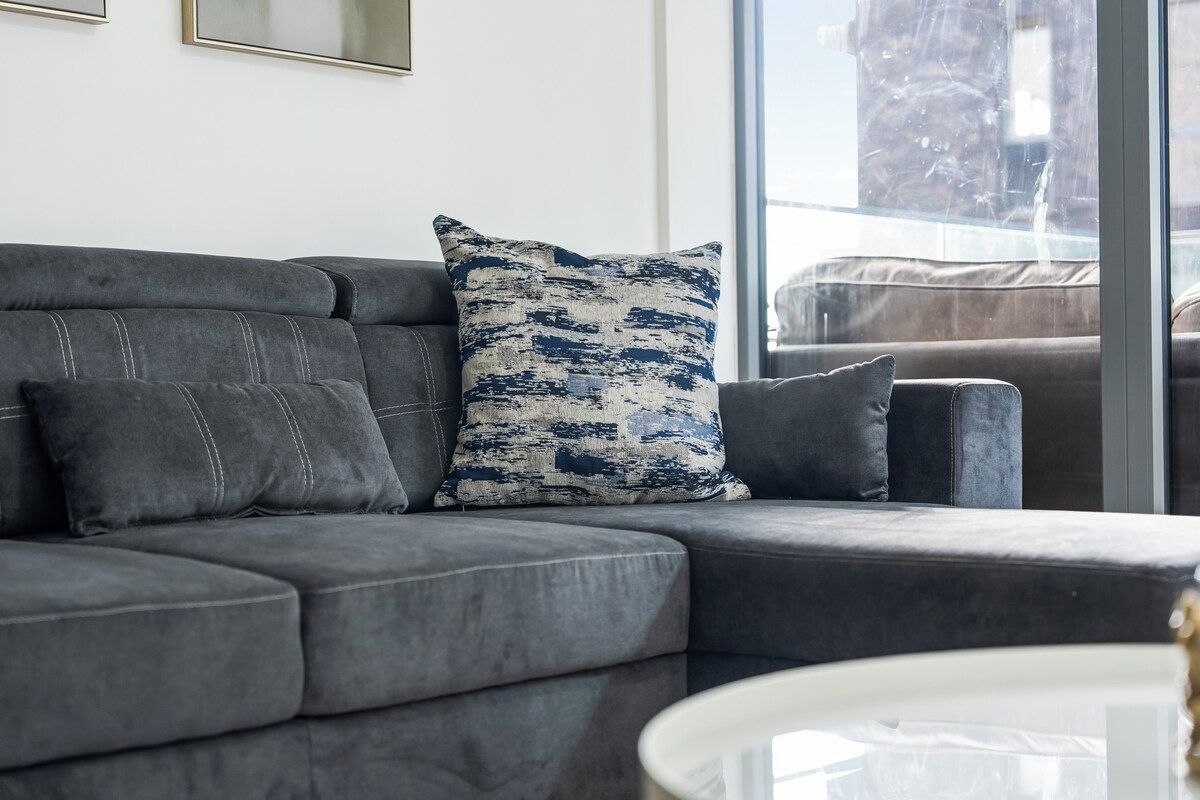 Un canapé d’angle gris avec un coussin à motifs et une table basse blanche dans un salon moderne.
