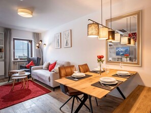 A modern living room with a dining area, featuring a sofa, a coffee table, a dining table set for two, and a large mirror on the wall. - Bergschlossel WHG 19 (Oberaudorf)