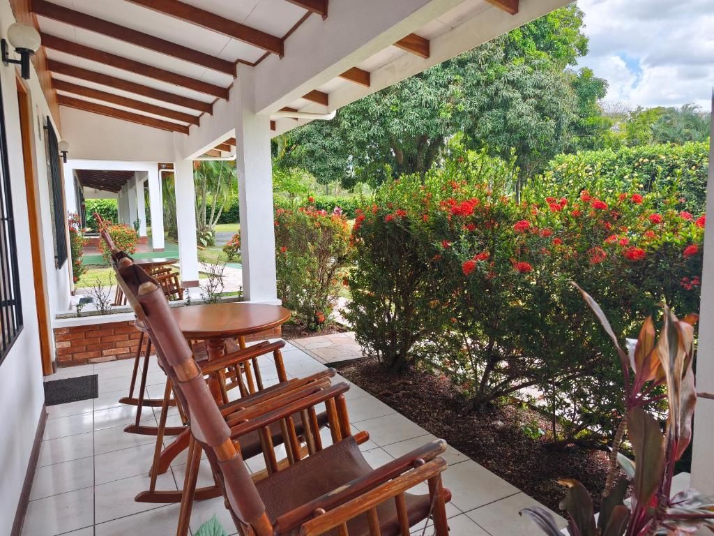 Área de estar coberta ao ar livre, com móveis de madeira e vista para um jardim com flores vermelhas.