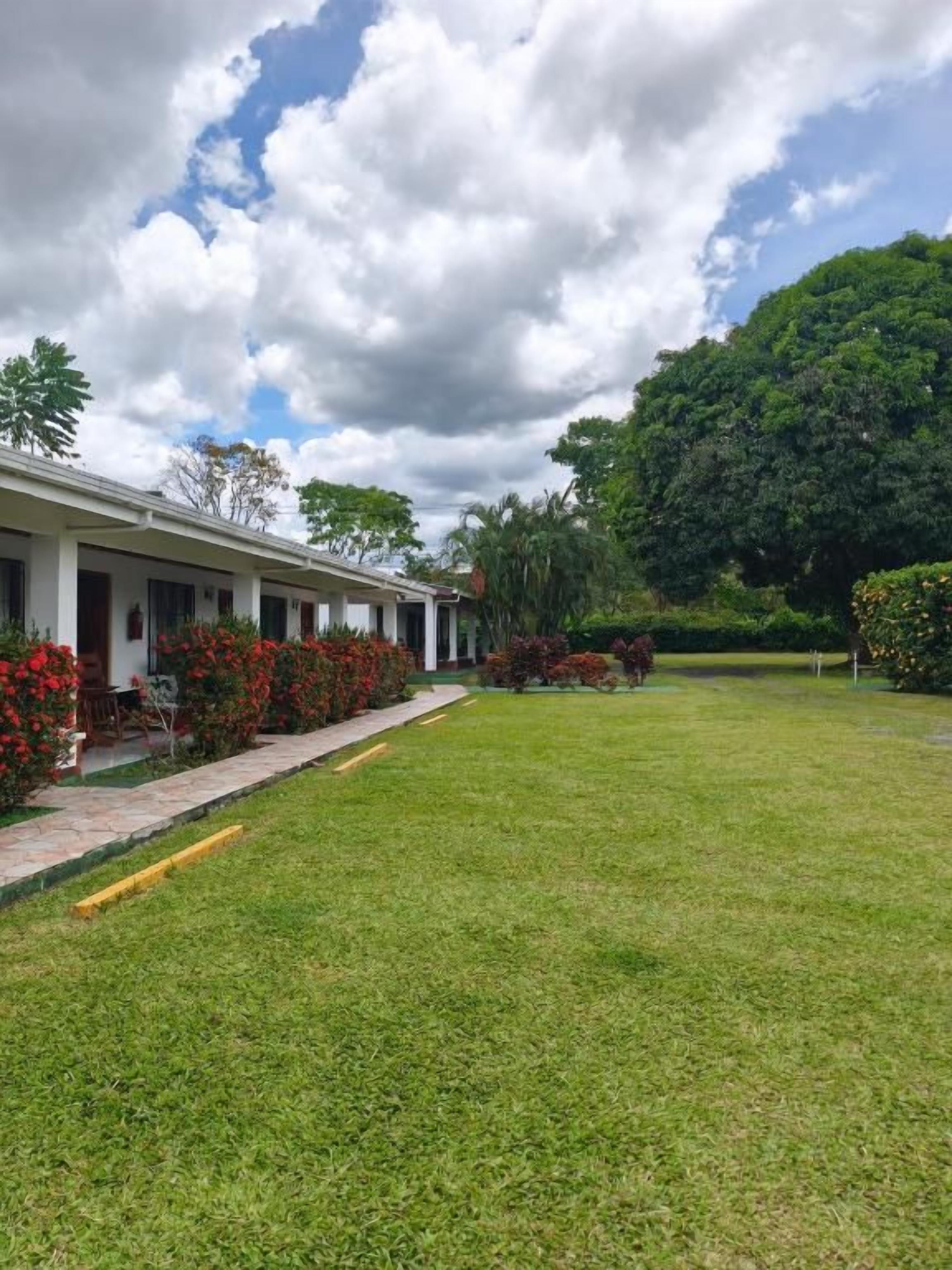 Hotel com gramado, prédio com varanda e uma grande árvore ao fundo.
