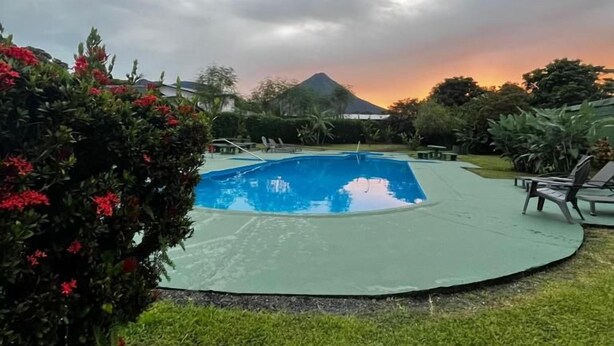 A swimming pool surrounded by greenery and a mountain in the background. - Hotel Villa Fortuna (La Fortuna)