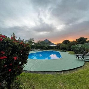 A swimming pool surrounded by greenery and a mountain in the background.