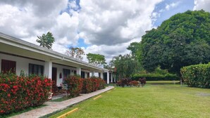 A hotel with a covered outdoor seating area, a well-maintained lawn, and a large tree in the background. - Hotel Villa Fortuna (La Fortuna)