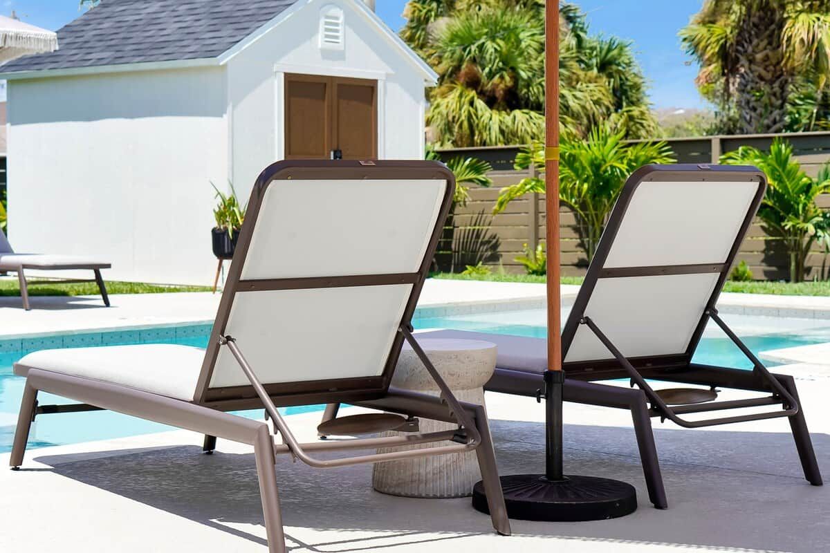 Two lounge chairs by a poolside with a white building and palm trees in the background.