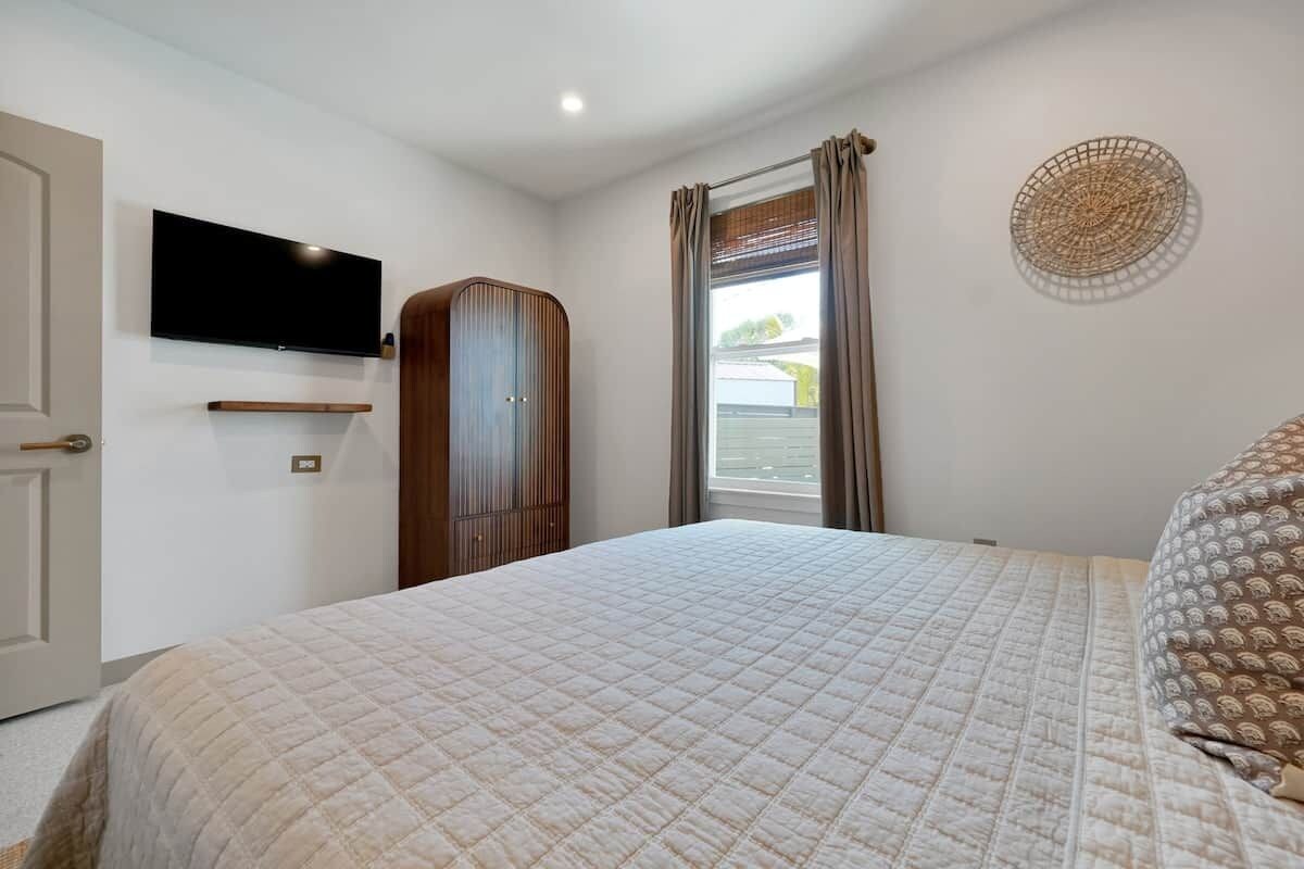 A bedroom with a bed, a television mounted on the wall, a wardrobe, and a window with curtains.