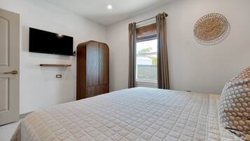 A bedroom with a bed, a television mounted on the wall, a wardrobe, and a window with curtains.