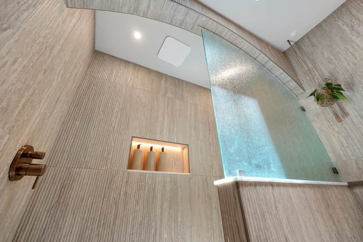 A modern bathroom with a curved glass shower enclosure, a built-in towel rack, and a recessed light fixture.