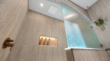 A modern bathroom with a curved glass shower enclosure, a built-in towel rack, and a recessed light fixture.