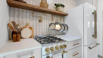 Een keuken met een gasfornuis, witte kasten en een witte koelkast.