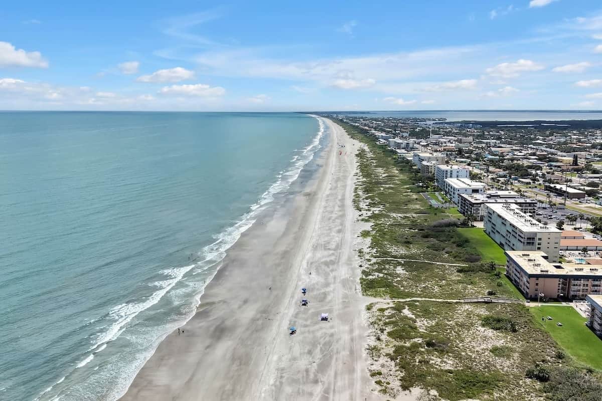 Un paysage urbain côtier avec une longue plage, des bâtiments et un ciel dégagé.