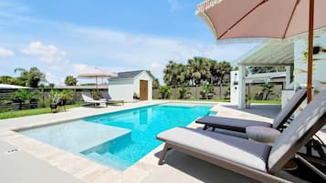 Ein Pool mit Liegestühlen und Sonnenschirmen, umgeben von einer Umzäunung und Palmen.